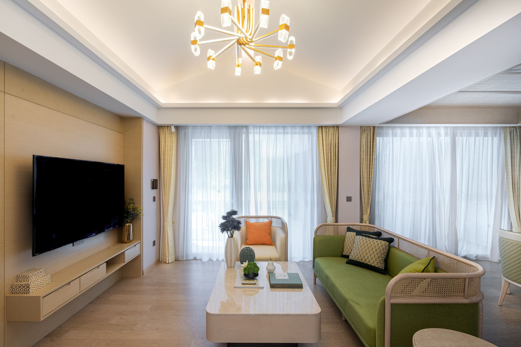 Salon moderne avec lustre doré, canapé vert et grandes fenêtres